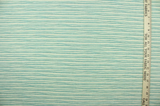 This fabric features brushstroke stripes design in a light blue set against a off white background . 
