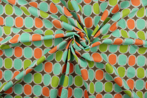 This fabric features a geometric design in bright orange, lime green, and turquoise outlined in white and set against a brown background. 
