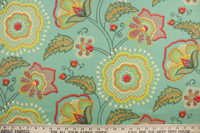 This fabric features a floral design in  green, orange, cream, dark pink, yellow and dark gray against a blue green.