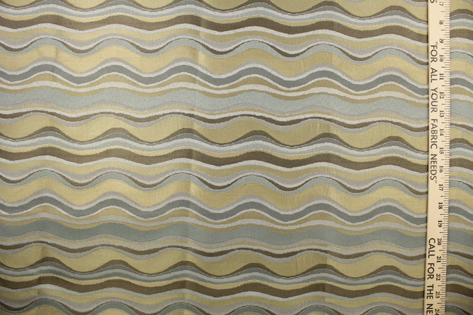  This fabric features a wavy design in gray, blue, taupe, and gold with a latex backing.