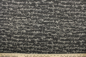 This fabric features a script design of kind words in cream against a dark gray background .