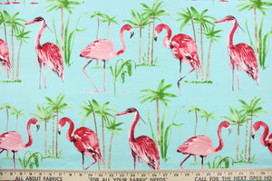 This outdoor fabric features a flamingo and tree design in green, pink, light brown, white and black against a light blue . 