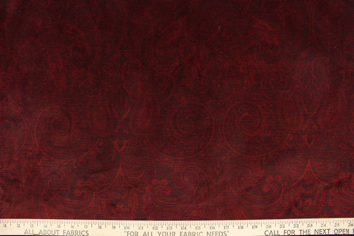  This velvet features a muted paisley design in a tone on tone burgundy .