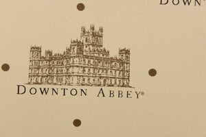 Featuring the downtown abbey building and wording in brown and black with brown dots against a tan background. 