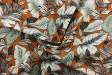 Load image into Gallery viewer, This Solarium outdoor print features a large tropical leaf design in black, gray, white and light green on a dark orange background.  This versatile, long-lasting fabric can withstand up to 500 hours of sunlight, water and stain resistant and has 10,000 double rubs.  It is perfect for lounge cushions, pool furniture, tablecloths, decorative pillows and upholstery projects.  This fabric has a slightly stiff feel but is easy to work with.  
