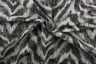 On the Prowl is a stylish upholstery fabric that features a unique abstract chevron pattern in black and linen colors. With a testing score of 25,000 double rubs, the fabric is abrasion and wear-resistant, providing long-lasting durability and quality over time.