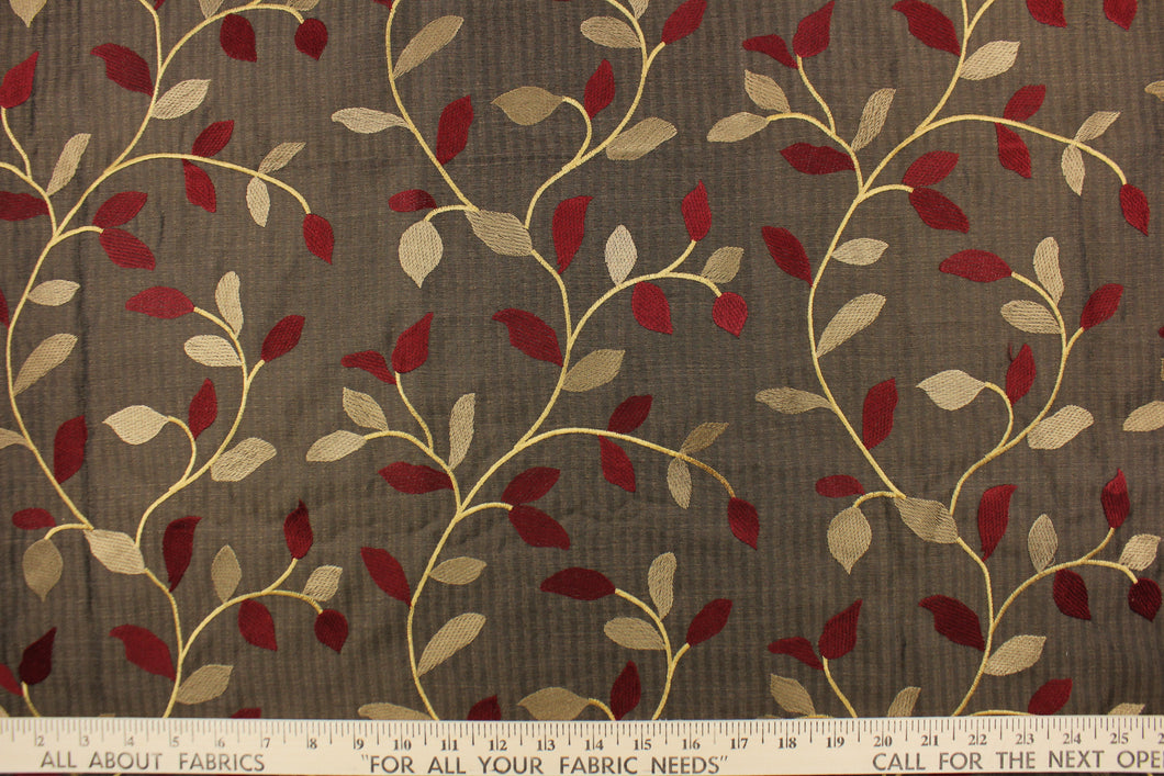  This fabric features a embroidery vine and leaf design in dark red, gold and tan against a dark brown . 
